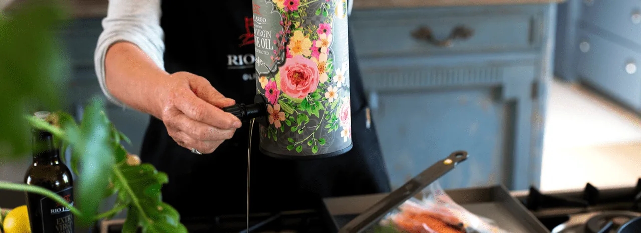 Olive oil being poured from a floral Rio Largo decanter into a pan